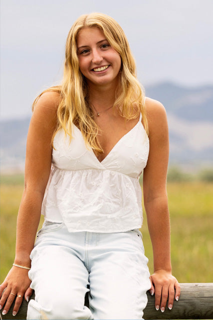 Allie, Broadwater Hot Springs swim instructor in a white top and light blue jeans sitting outdoors with mountains in the background.